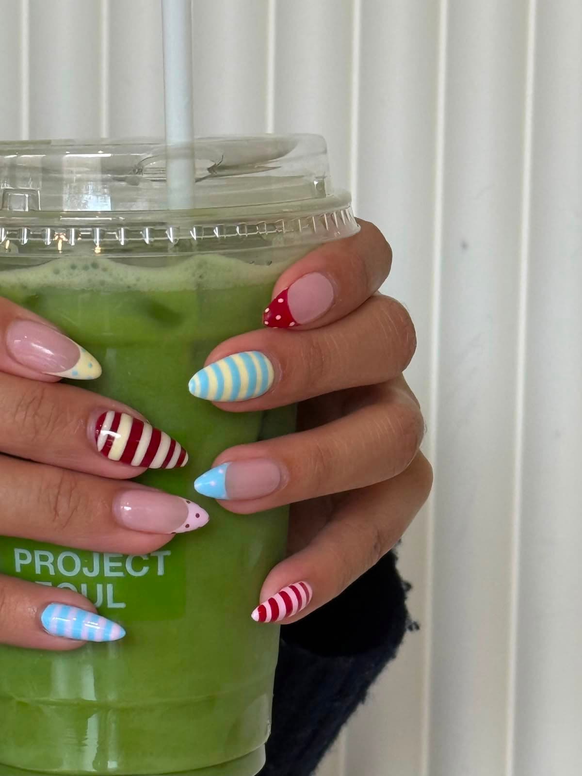 Uñas cortas con rayas de caramelo en rojo, azul y amarillo y puntas de lunares